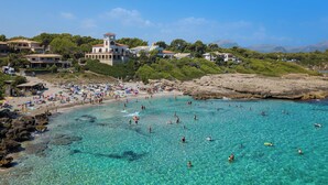 Eine Küstenlandschaft mit klarem türkisblauem Wasser, einem Sandstrand und Gebäuden im mediterranen Stil.