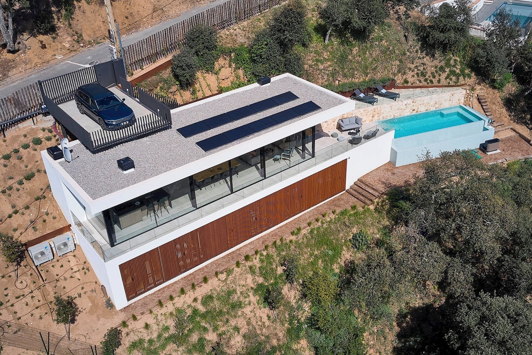 A modern house with a flat roof, large glass windows, a swimming pool, and a covered patio area.