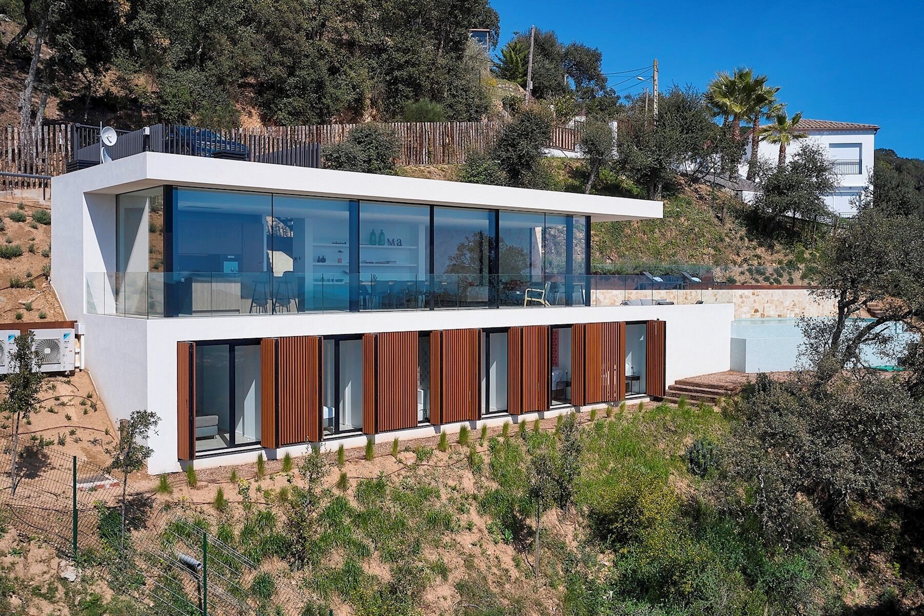 Una casa moderna de dos pisos con amplios ventanales, techo plano y terraza de madera.