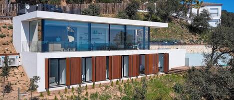 Una casa moderna de dos pisos con amplios ventanales, techo plano y terraza de madera.