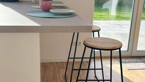 Une cuisine moderne avec une grande fenêtre, un plan de travail blanc, un saladier rose et un vase rempli de fleurs.