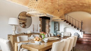 A dining area with a wooden table, white chairs, and a chandelier. There is a staircase leading to an upper level. - Mas del Suro -  Masia in the heart of Costa Brava (Mont-ras)