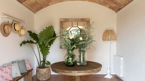 A room with a round wooden table, a bench with cushions, a large potted plant, two glass vases with flowers, a mirror, and a lamp. - Mas del Suro -  Masia in the heart of Costa Brava (Mont-ras)