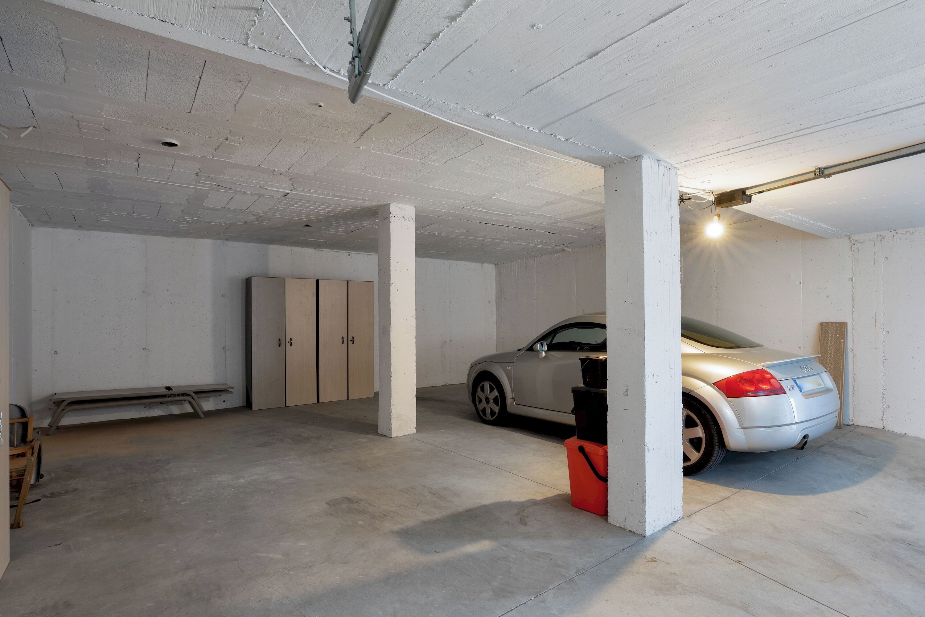 Een parkeergarage met een auto nabij een pilaar, een betonnen vloer en witte muren.