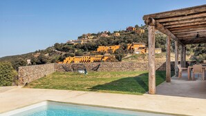 Un espace piscine agrémenté d’une pergola et de mobilier d’extérieur, entouré d’un mur de pierre et offrant une vue sur les maisons situées sur les flancs de la colline.