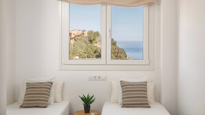 Une chambre avec deux lits, une vue sur la mer et une petite plante en pot.