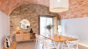Un coin repas agrémenté d’une arche en pierre, d’une table en bois, de chaises blanches et d’un buffet en bois.