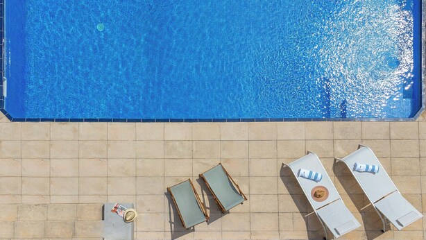 Ein Schwimmbecken mit gefliesten Rändern und Liegestühlen.