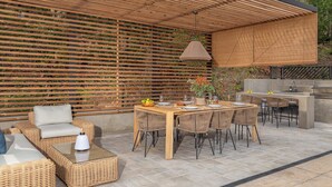 Eine Terrasse im Freien mit einem Holztisch, Stühlen, einer gewobenen Couch und einer hängenden Leuchte.