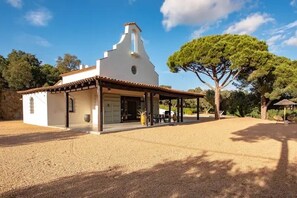 A white building with a tiled roof, a covered porch, and a large tree in the background. - Casa La Capella - Lovely property with pool in Costa Brava (Girona)