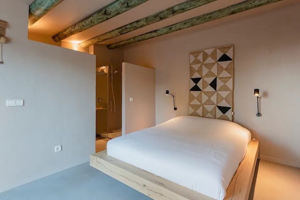 A bedroom with a bed, a geometric wall decoration, and a wooden ceiling beam.