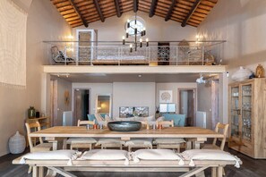 Un vaste espace dédié à la salle à manger, avec une grande table en bois, de nombreuses chaises et un centre de table décoratif en forme de bol.