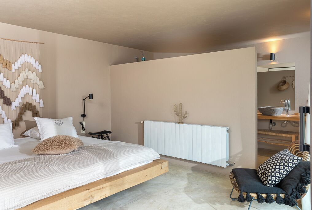 Een slaapkamer met een bed, nachtkastje, lamp en een stoel.