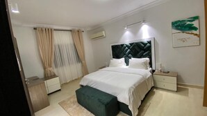 A modern bedroom with a large bed, a bedside table, a nightstand, a bench, and a wall-mounted air conditioner. - Charming and Spacious 3 Bed in Lekki Phase1 (Lekki)