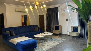 A living room with a blue sofa, a round coffee table, and two armchairs. There is a floor lamp, a mirror, and a plant. - Charming and Spacious 3 Bed in Lekki Phase1 (Lekki)