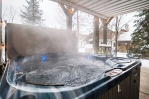 A hot tub with a cover, steam rising, and a wooden deck in the background.