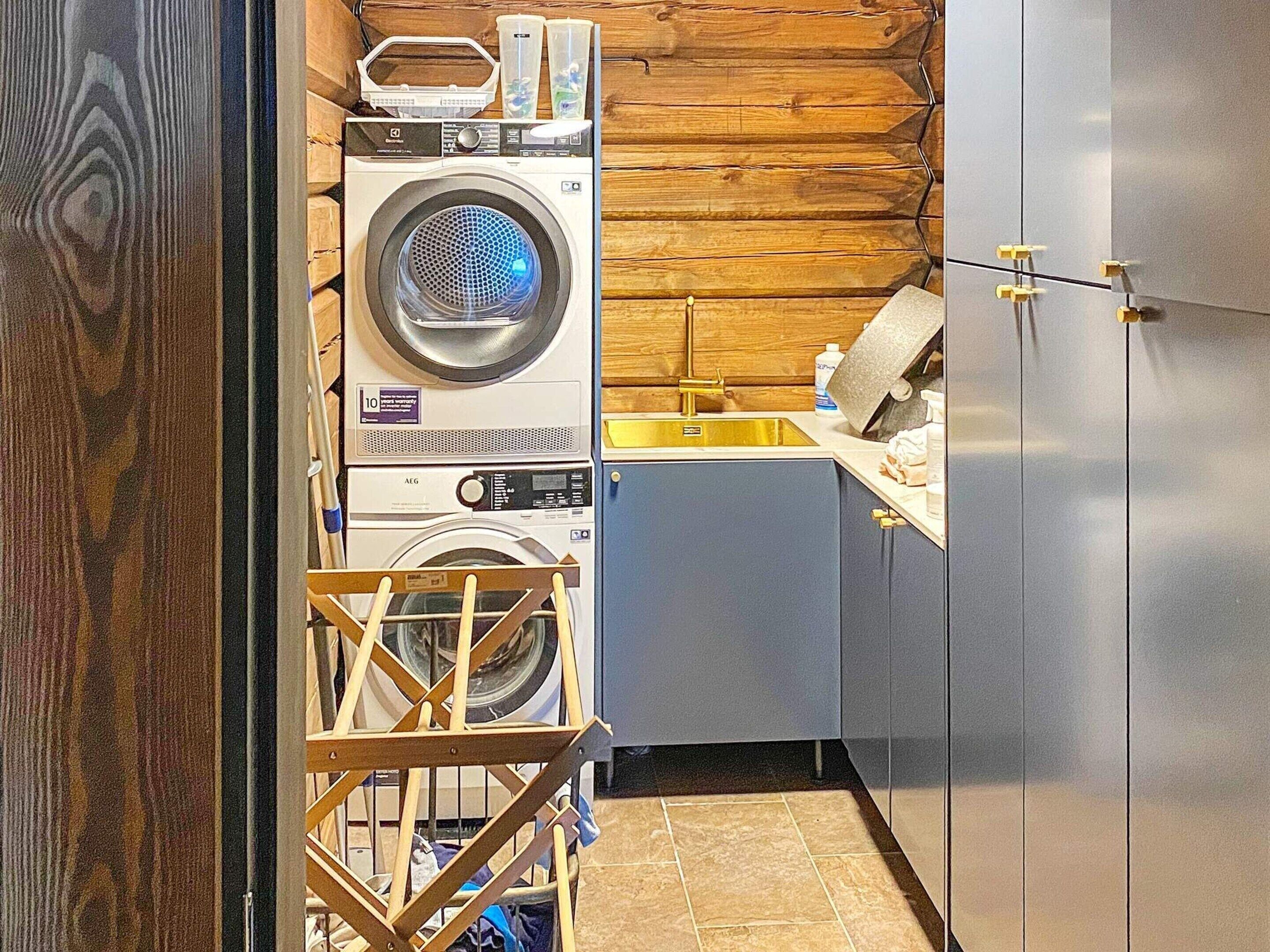 Een wasruimte met gestapelde wasmachines, een droogrek en een wasbak.