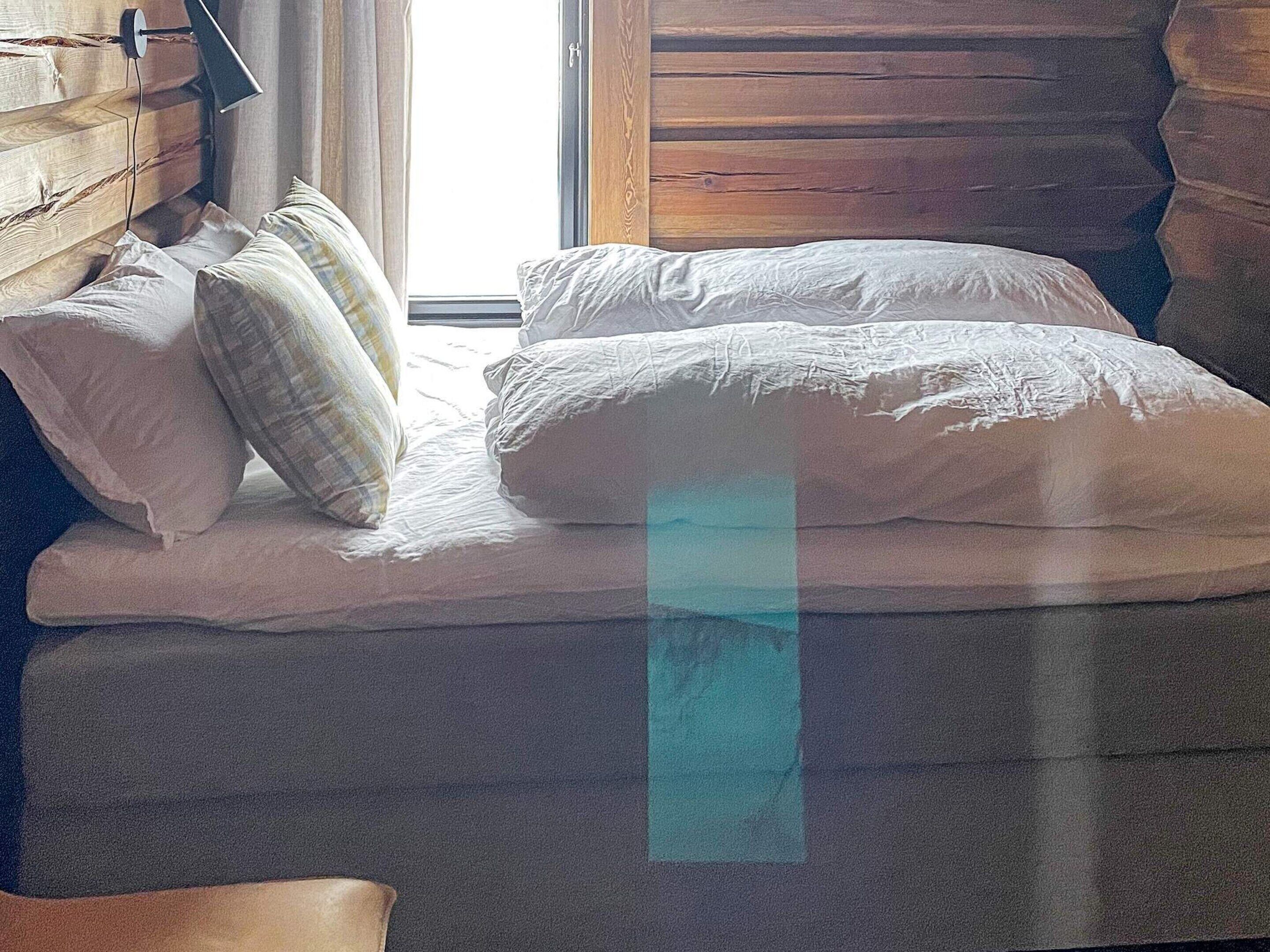 A bed with white bedding and a wooden headboard, a window with curtains, and a wooden wall.