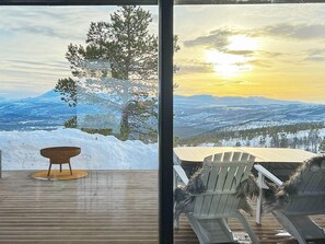 A deck with a wooden chair and a small table, overlooking a snowy landscape with a mountain and a sunset view. - 10 Person Holiday Home in Moen-by Traum (Målselv)