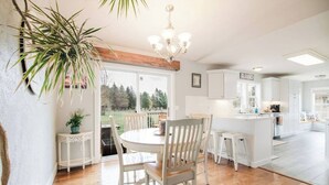 A modern kitchen with white cabinetry, a dining area with wooden chairs, and a large window overlooking a garden. - G's: Pet friendly: Firepit: King bed: Walk2town (Boyne City)