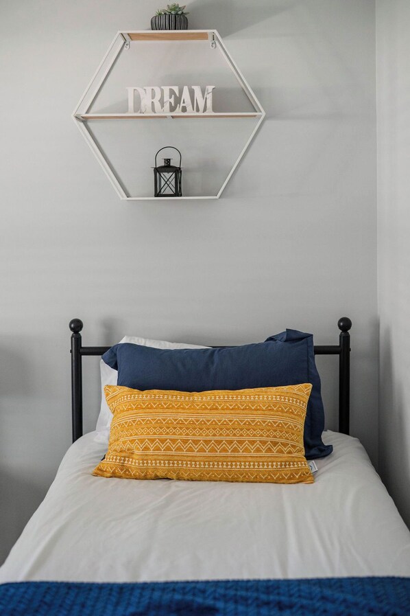 A bedroom with a bed, a hexagonal wall decoration with the word "DREAM" and a lantern, and a black metal headboard.