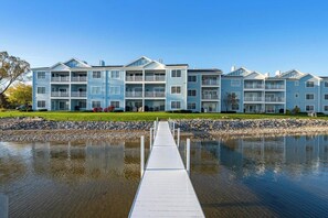 A multi-story residential building with balconies, a dock leading to a body of water, and a well-maintained lawn.