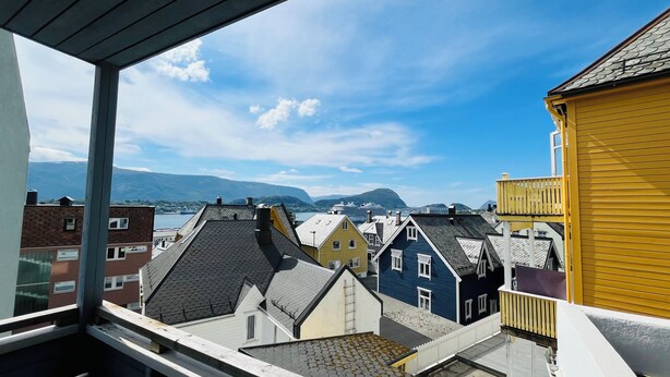 Une vue depuis une fenêtre donnant sur des bâtiments aux couleurs vives et sur une étendue d’eau, avec des montagnes à l’horizon.