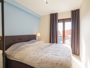 Een slaapkamer met een bed, nachtkastje, lamp en raam met gordijnen.