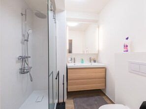 Een moderne badkamer met een douchecabine van glas, een houten wastafelmeubel en een witte wasbak.