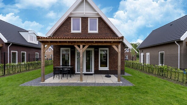 Une maison à deux étages dotée d’un patio couvert, d’une façade en briques et d’une pelouse bien entretenue.