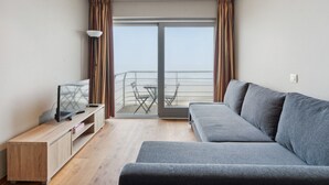 Un salon moderne avec un canapé gris, un meuble TV en bois et un balcon agrémenté d’une table et de chaises.