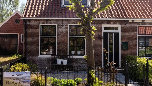 A traditional brick building with a tiled roof, large windows, and a small tree in the front yard.