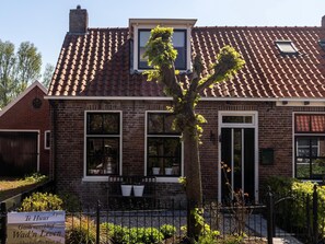 Une maison en briques avec un toit en tuiles, une petite fenêtre et une enseigne devant.