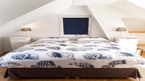 A bedroom with a sloped ceiling, a bed with a patterned bedspread, two bedside tables with lamps, and a window.