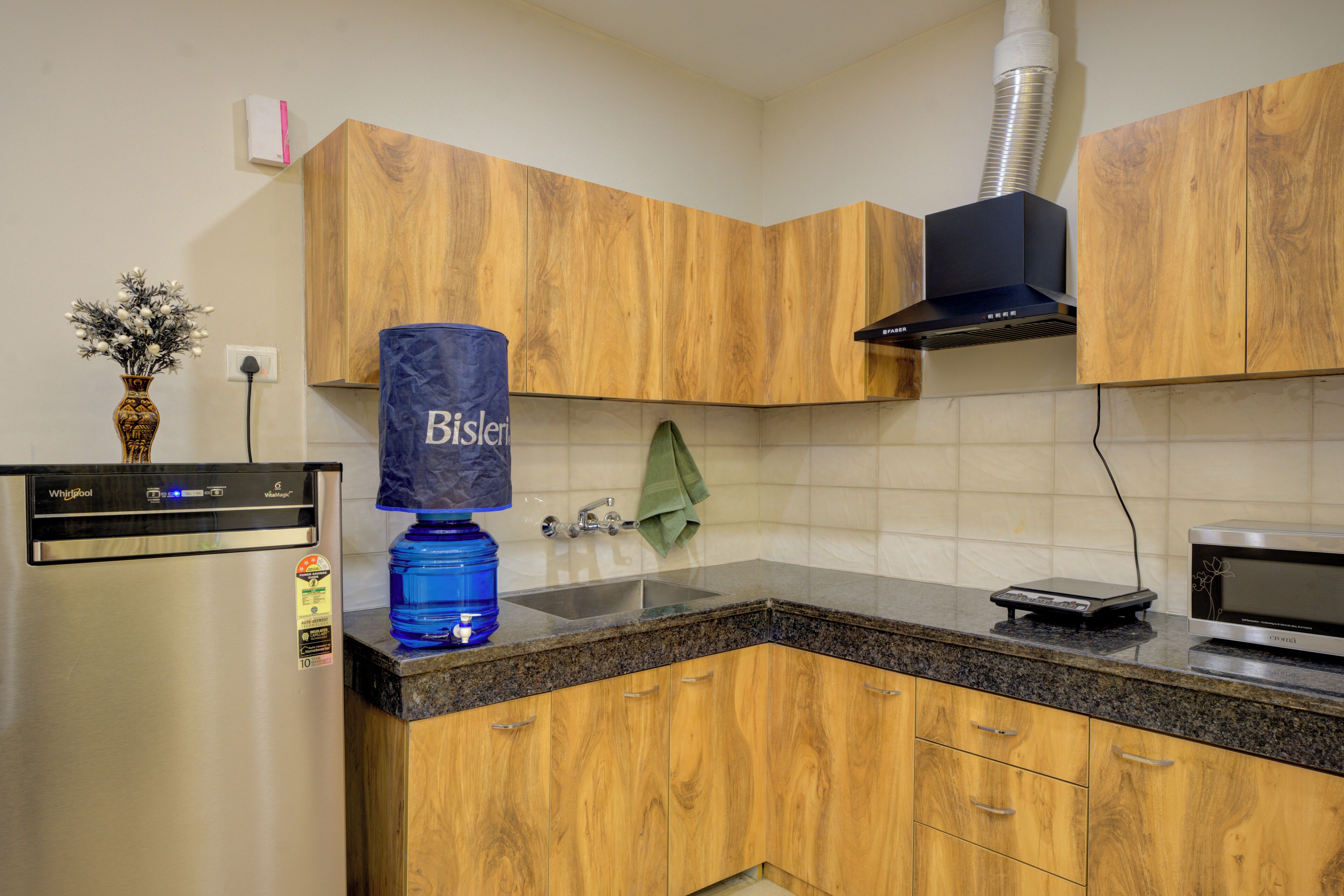 A kitchen with wooden cabinets, a stainless steel refrigerator, a water dispenser, a microwave, and a sink.