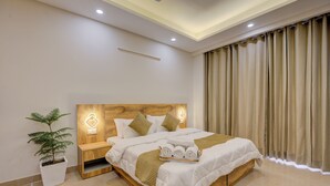 Une chambre d’hôtel moderne avec une tête de lit en bois, une table de chevet avec une lampe, une plante en pot et un lit bien fait, agrémenté de serviettes roulées.