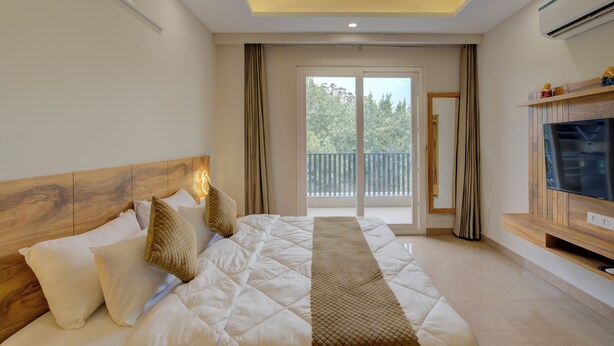 Une chambre moderne avec un grand lit, une télévision et un balcon donnant sur la verdure.