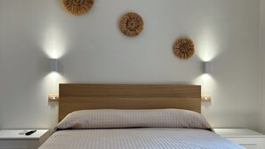A neatly made bed with a quilted cover, a wooden headboard, and three wall-mounted light fixtures with circular wall art above.