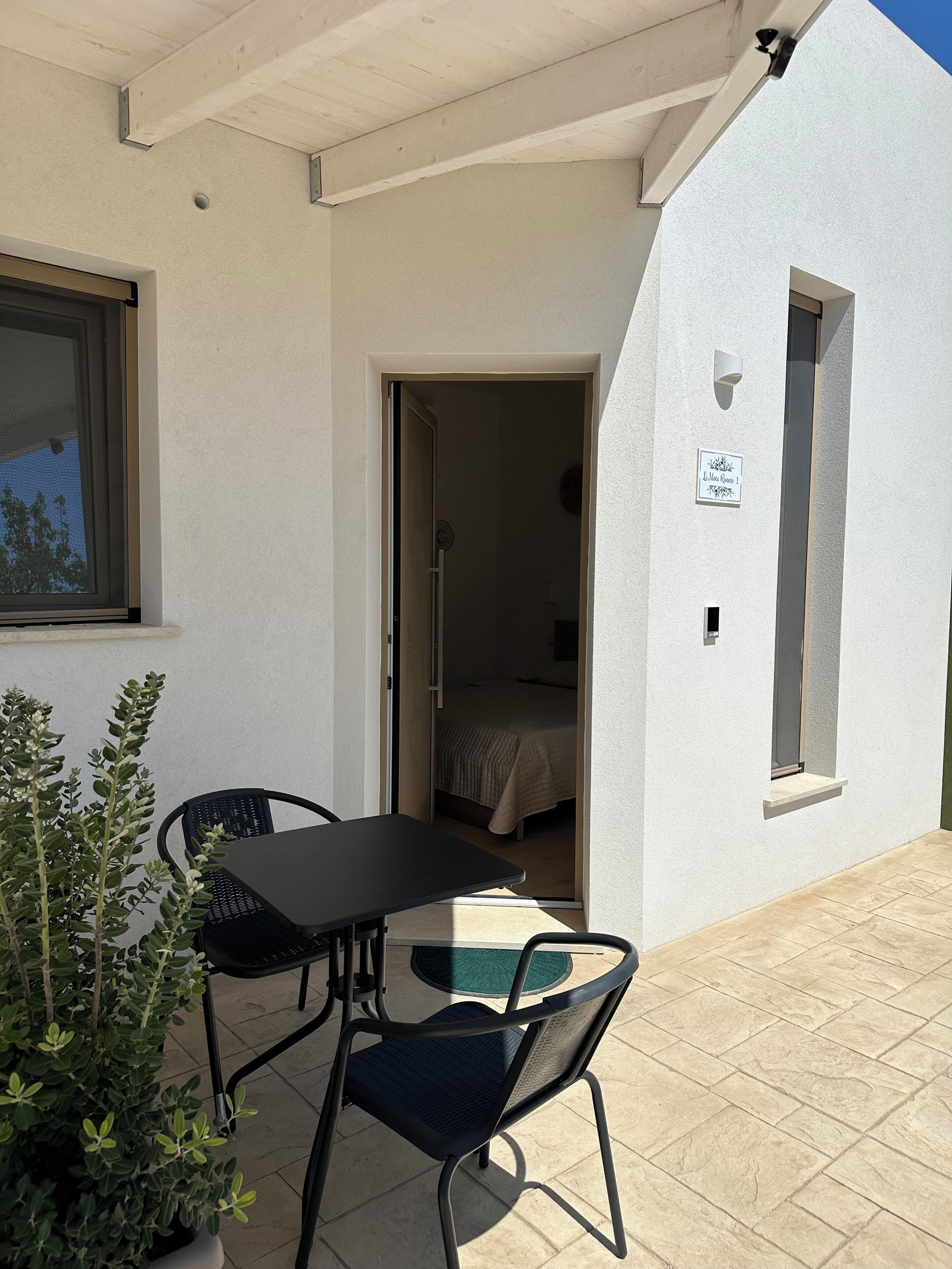 A small, single-room accommodation with a balcony, a table and chairs, and a potted plant.