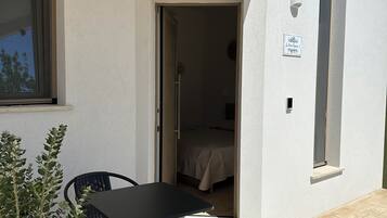 A small, single-room accommodation with a balcony, a table and chairs, and a potted plant.