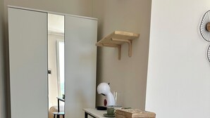 A compact kitchen with a white countertop, two stools, a white appliance, and a wooden shelf.