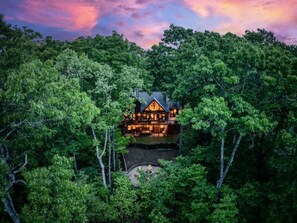 A lodge surrounded by dense forest, with a visible deck and outdoor seating area. - Western Sky - Lovely view, hot tub, fire pit, pets (Blue Ridge)