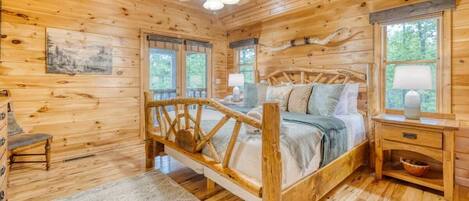 A wooden cabin bedroom with a bed, a nightstand, a chair, a ceiling fan, and windows.