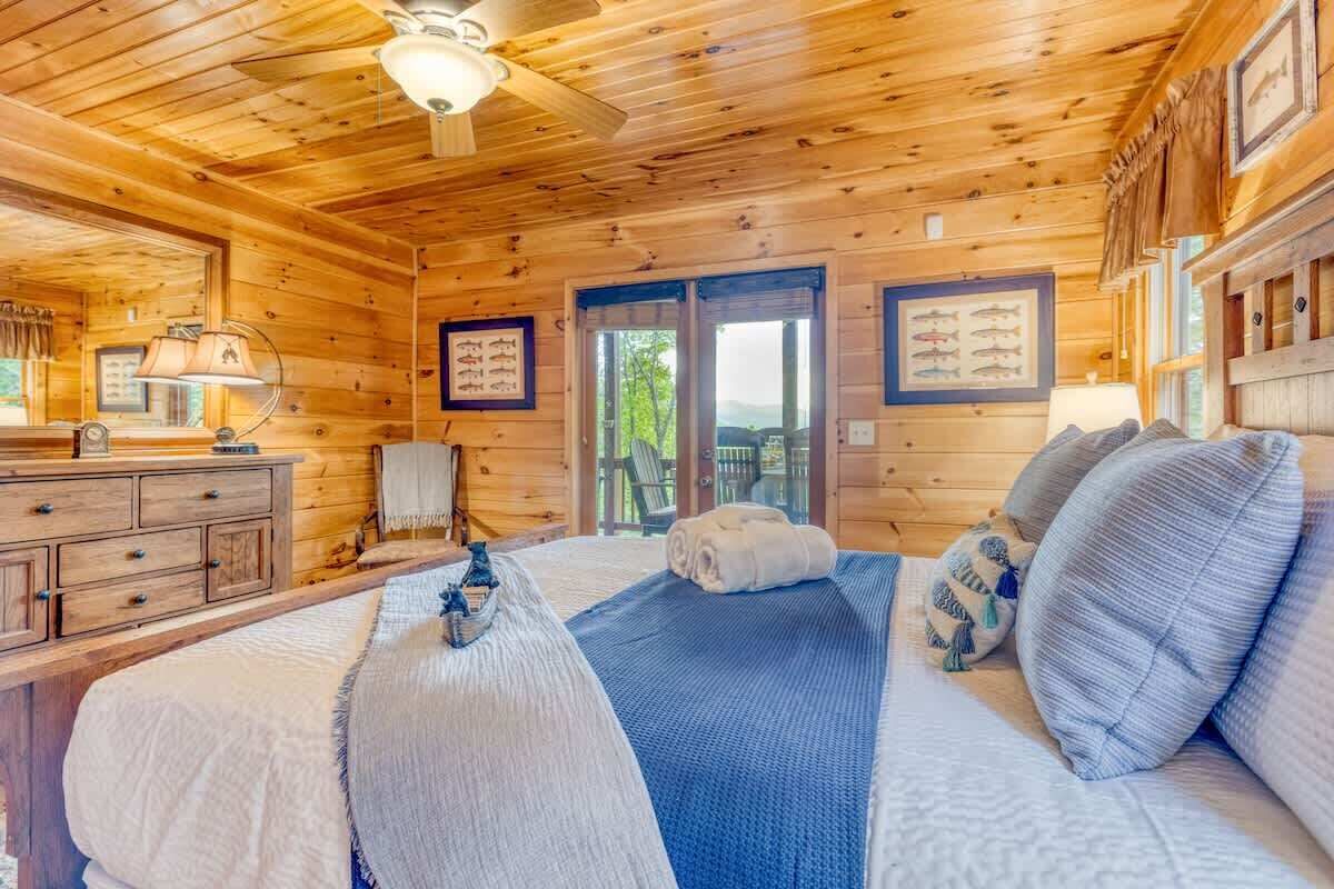 A wooden cabin room with a bed, a dresser, a ceiling fan, and framed pictures on the walls.