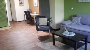 A modern living room with a grey sofa, a black armchair, and a coffee table. There is a dining area with a table and chairs in the background. - Holiday Apartment Langkamp (Neuenkirchen)