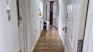 Un couloir étroit avec un plancher en bois, des murs blancs et des portes de chaque côté.