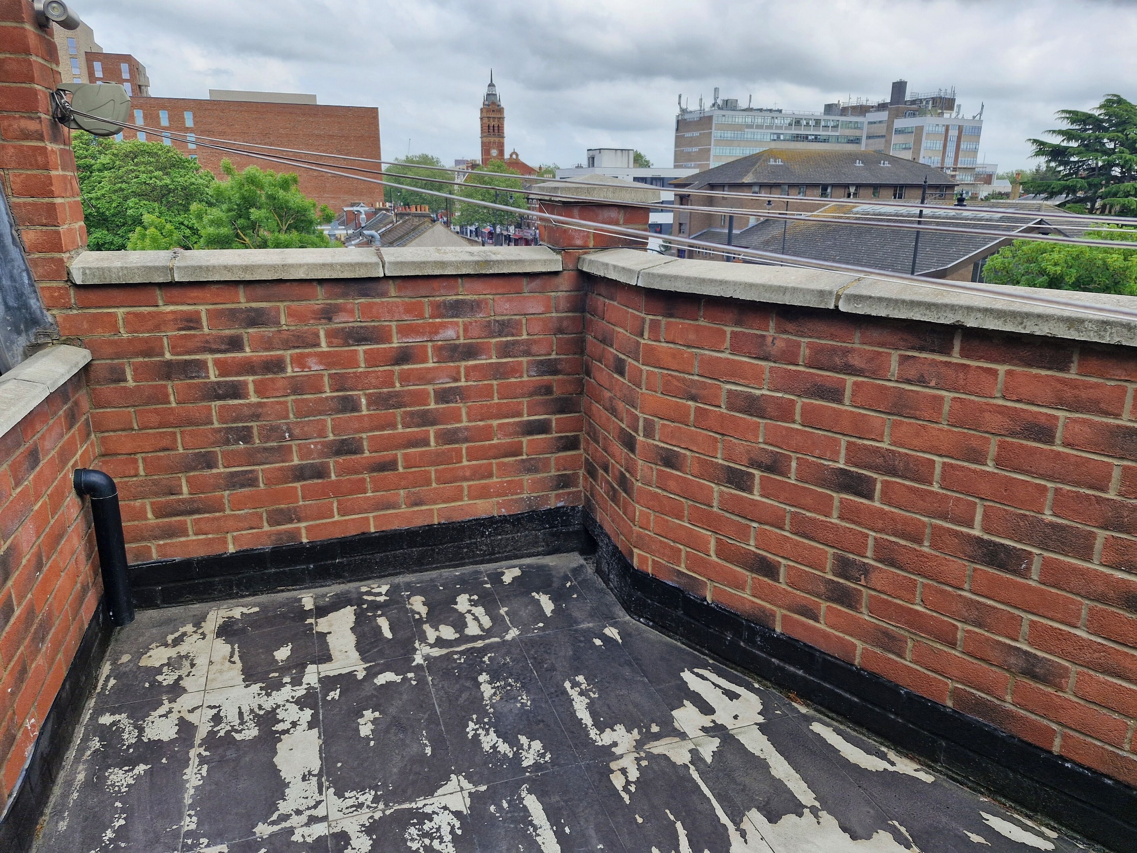 A rooftop with a brick wall, a black pipe, and a tiled floor with peeling paint.