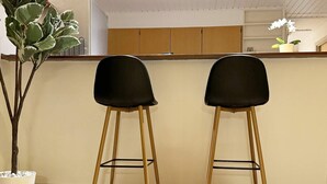 Deux tabourets de bar noirs avec des pieds en bois, dans un coin cuisine doté de meubles de rangement en bois et d’une plante en pot.