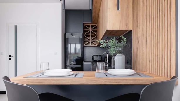 Un espace repas moderne avec une table en bois, des chaises noires et une cuisine en arrière-plan.