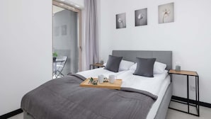 Une chambre d’hôtel moderne avec un grand lit, une table de chevet avec une lampe et une petite table sur laquelle se trouve un plateau avec des articles pour le petit-déjeuner.